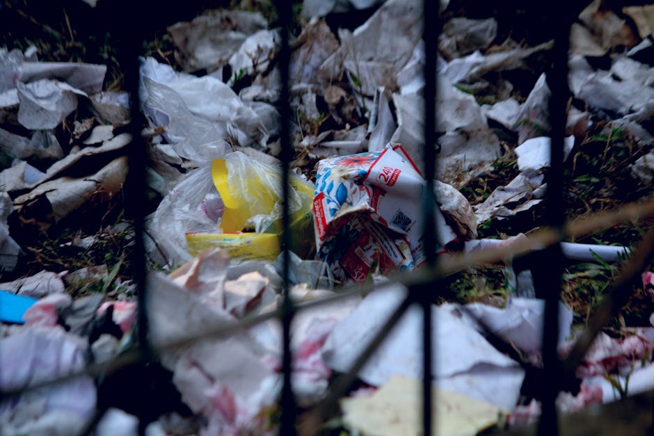 A discarded soda can lying on a rough, asphalt surface. The can is made of aluminum with a metallic finish, featuring pink and gold coloring around the top rim and body. The pull-tab is open, exposing